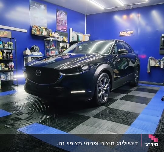רכב שחור בחדר דיטיילינג עם מוצרים על מדפים